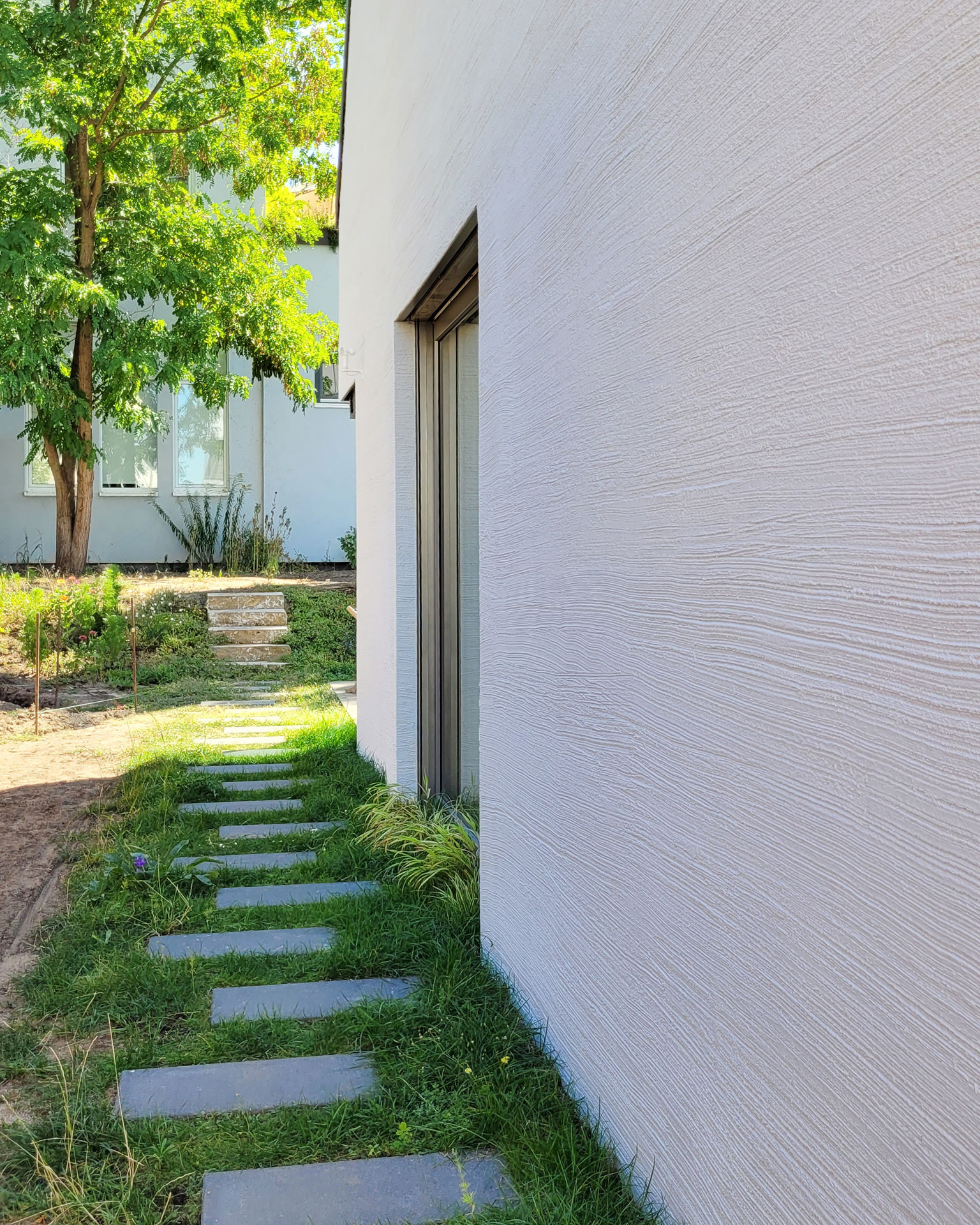 Seitlicher Gartenweg mit Rasenplatten entlang einer weißen Besenstrich-Fassade