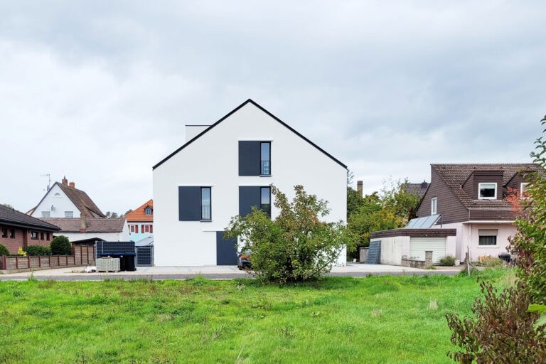 Straßenansicht von Haus TH1 mit weißer Fassade, dunklen Fensterläden und Satteldach